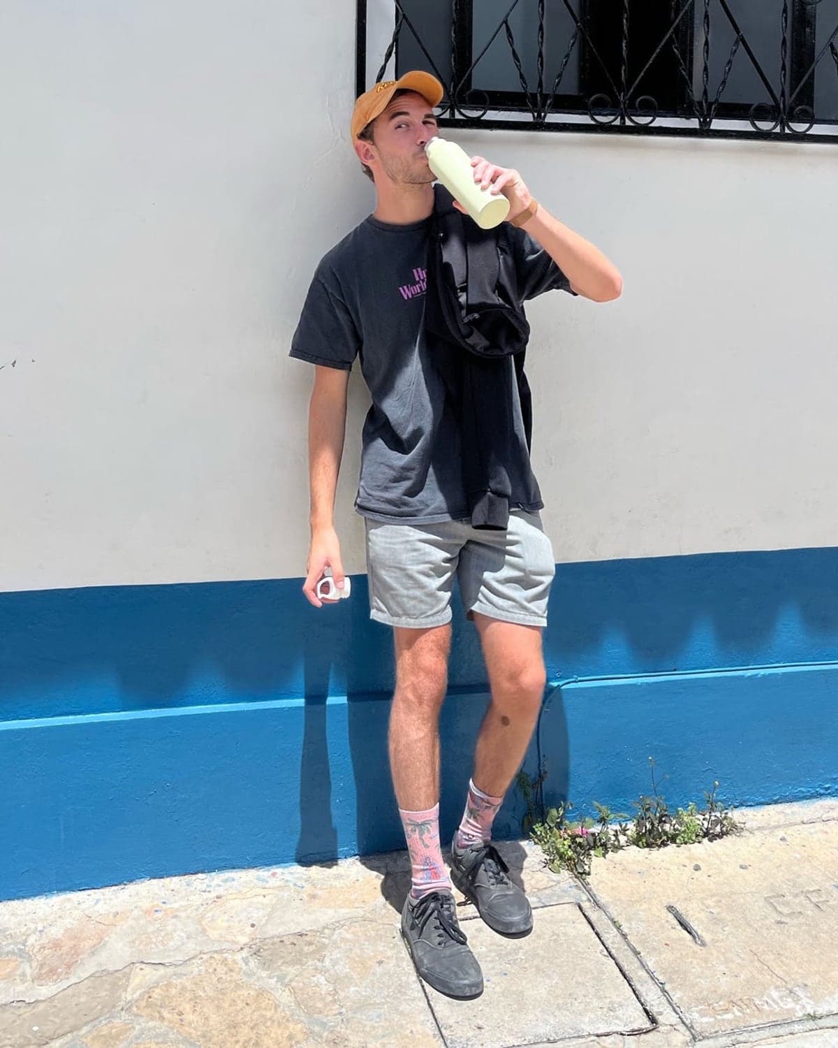 Roee Sivan, leaning against a white and blue painted wall on a sunny street